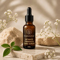 stone slab aur flowers wali: Razo Niyaz Intimate Firming & Care Serum 30ml amber dropper bottle on a stone slab with white flowers and green leaves.